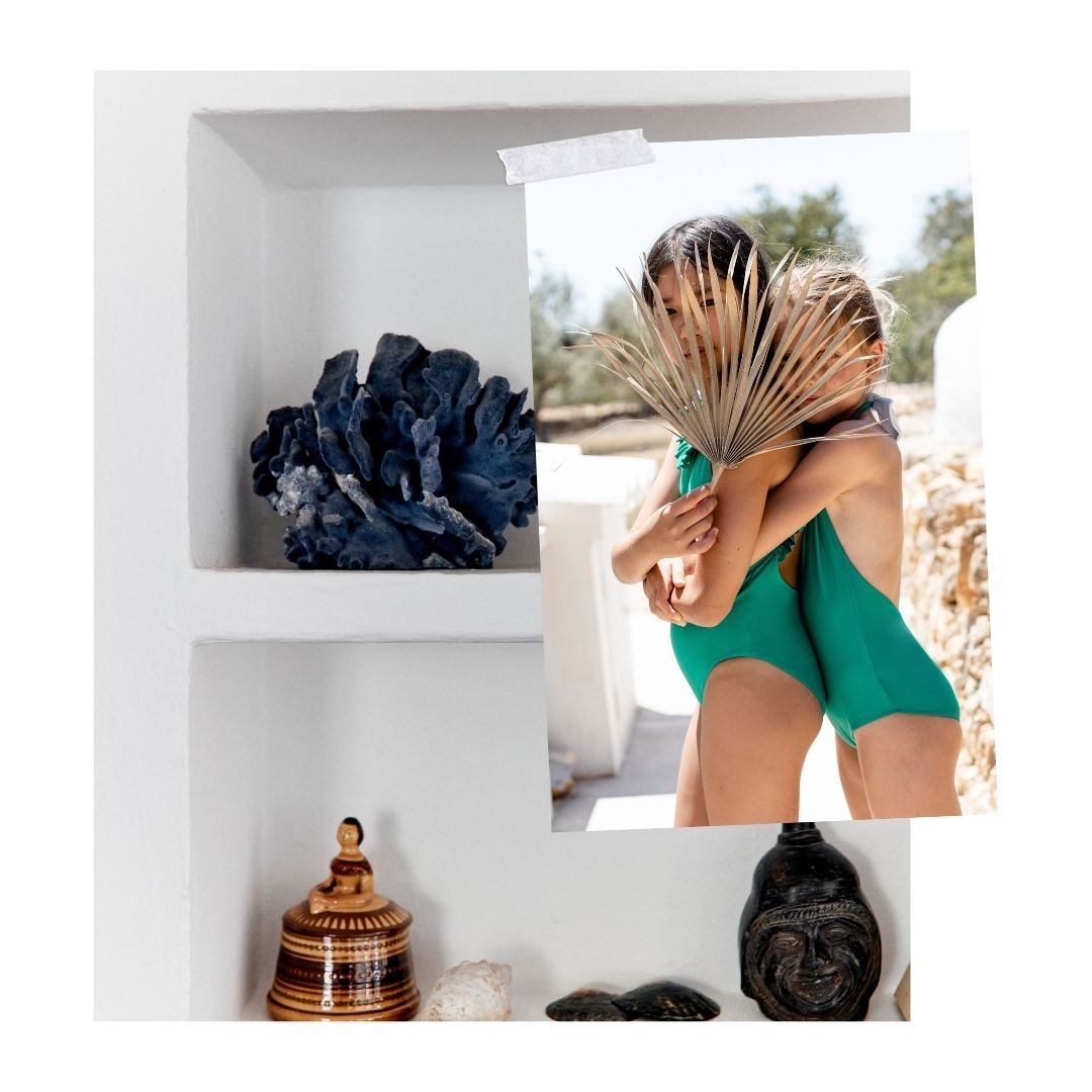Une étagère blanche minimaliste avec des objets décoratifs tels qu'un corail bleu foncé, une petite boîte en bois dorée et quelques pierres. Une photo superposée sur l’image avec deux filles portant des maillots en ton vert. Une des filles a une feuille dans la main qui couvre leur visages.